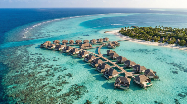 Aerial panorama of overwater villas across a turquoise lagoon and surrounding atoll.
